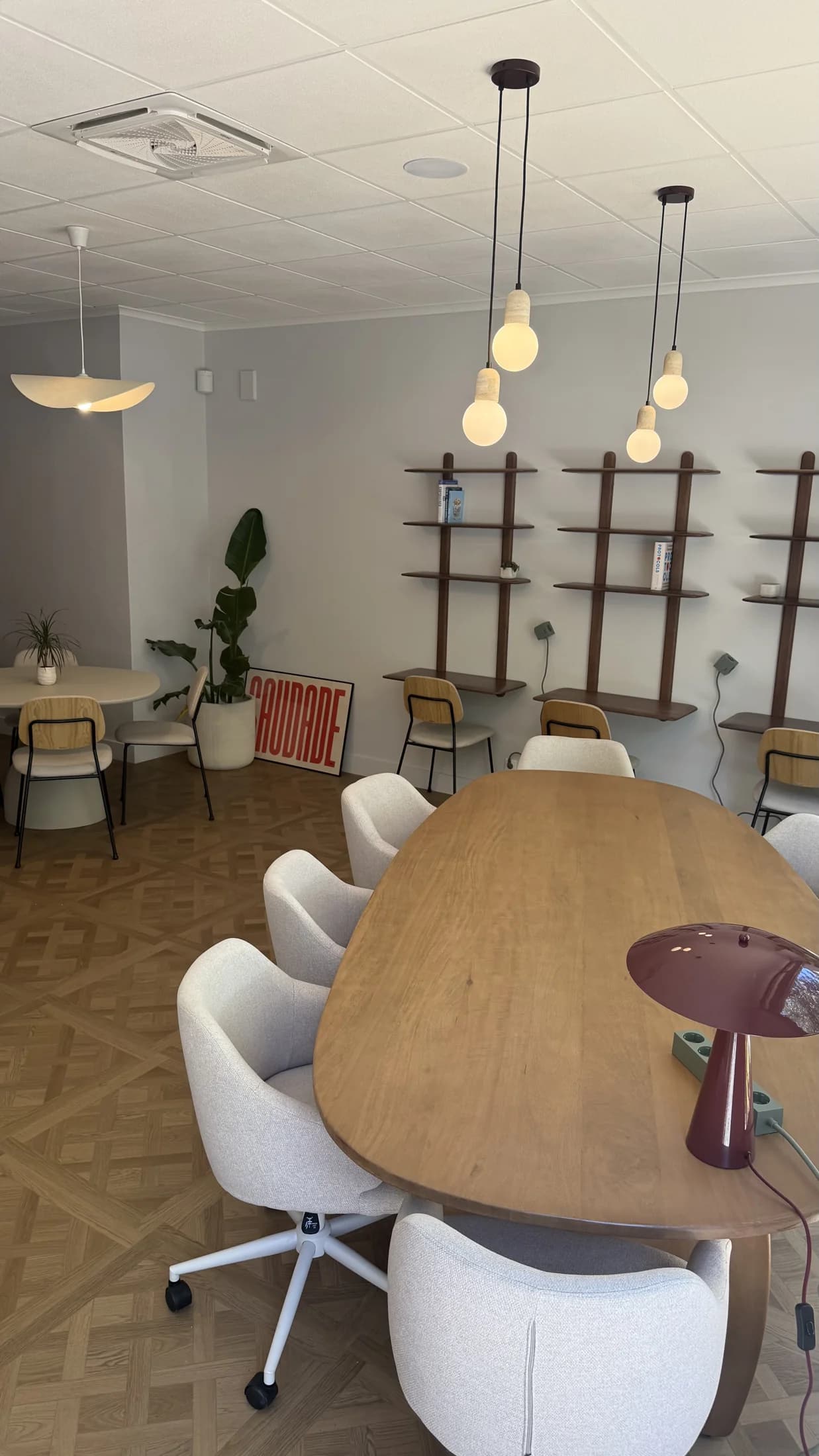 Mesa de madeira partilhada com cadeiras giratórias estofadas e candeeiros suspensos no Club Cowork